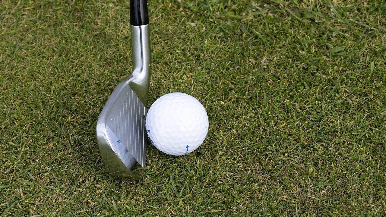 Golf iron resting next to a golf ball on short grass