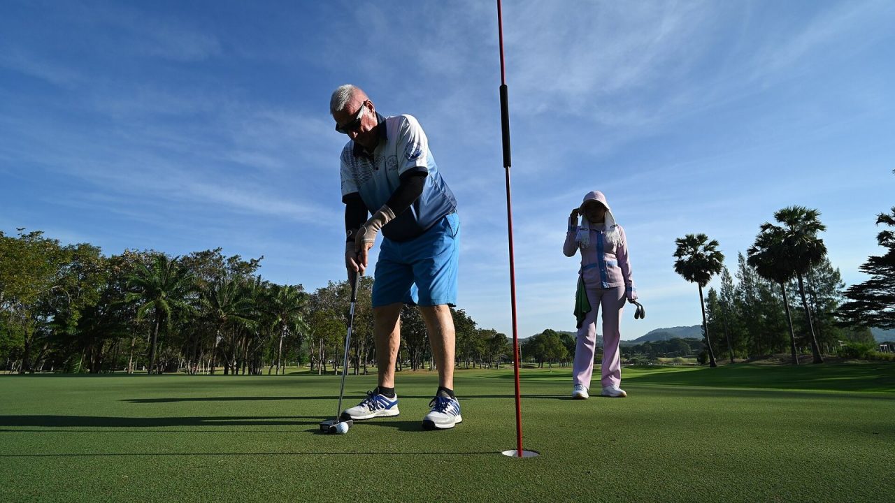 Golfer lining up a putt while his playing partner stands still nearby