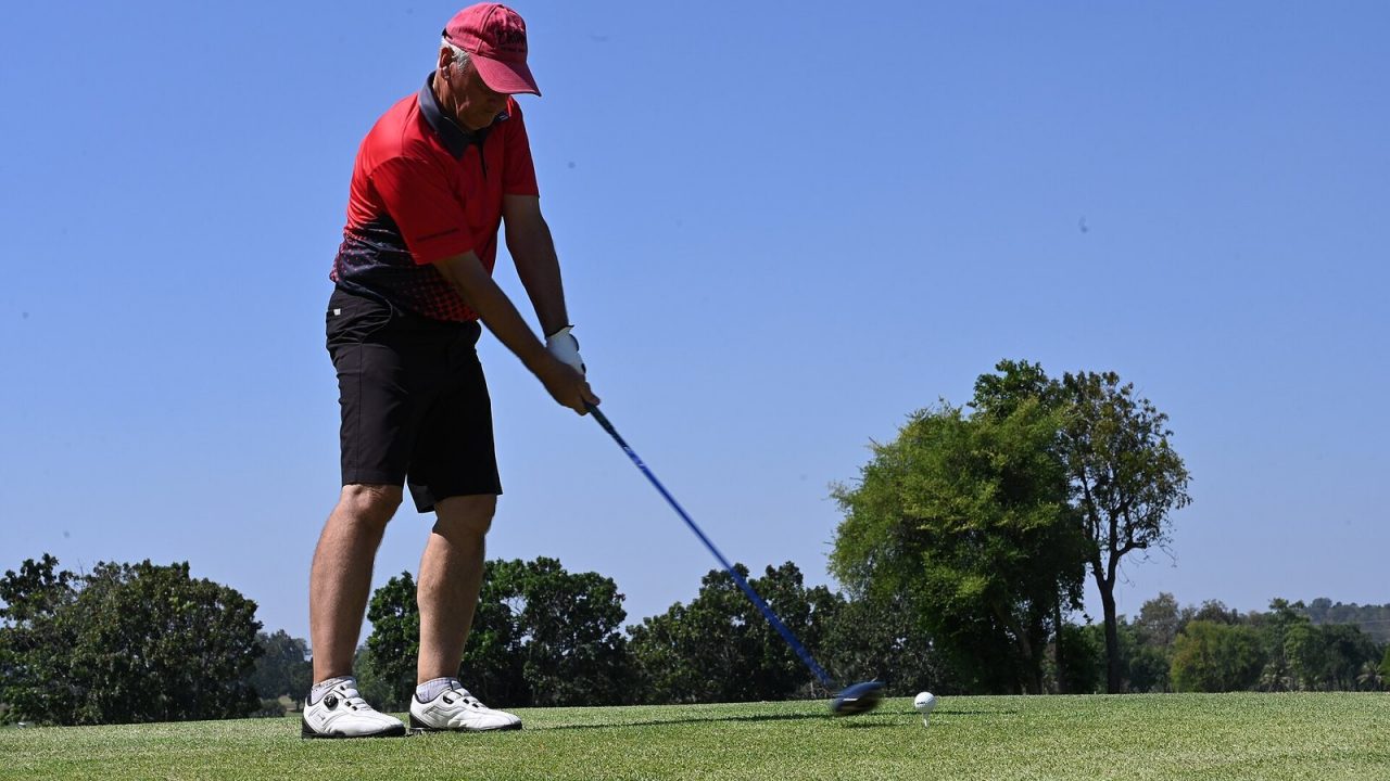 Golfer in a red shirt and cap at address on a tee box before a drive