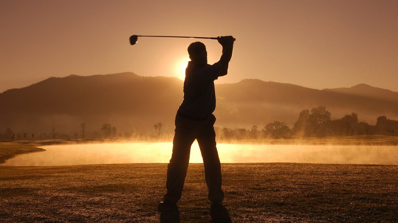 Silhouette of a golfer swinging at sunset