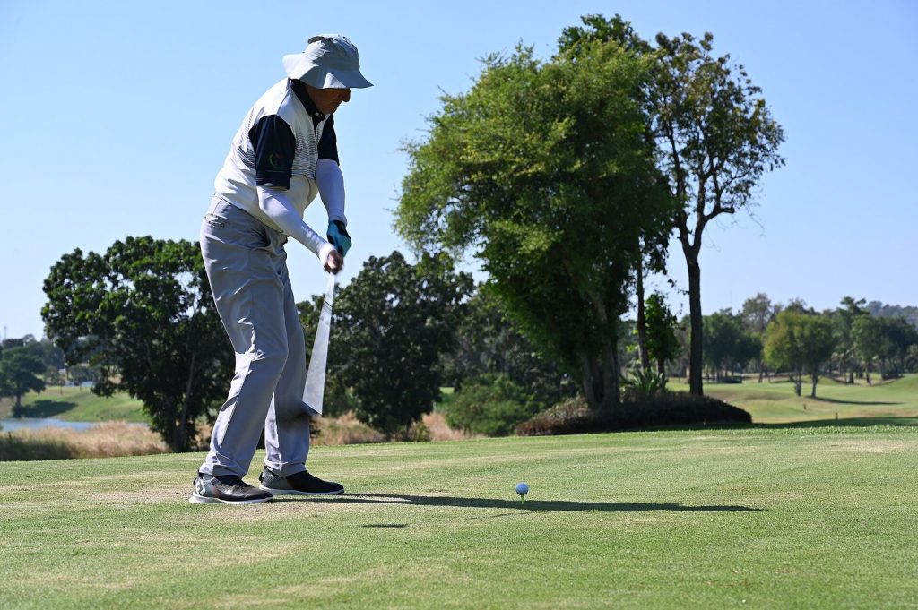 Golfer in a wide-brim hat swinging through on a tee shot