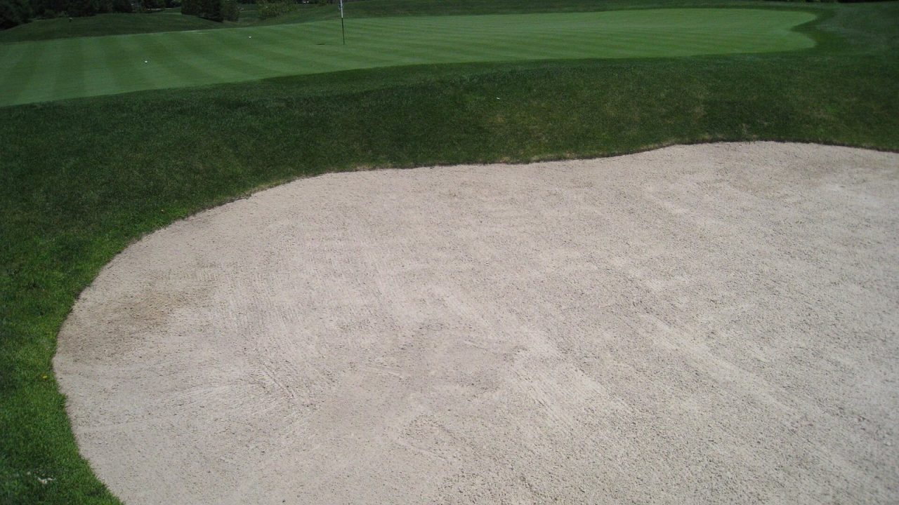 Raked sand bunker beside a golf green
