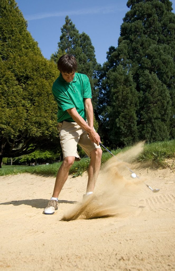 Golfer splashing a ball out of a greenside bunker